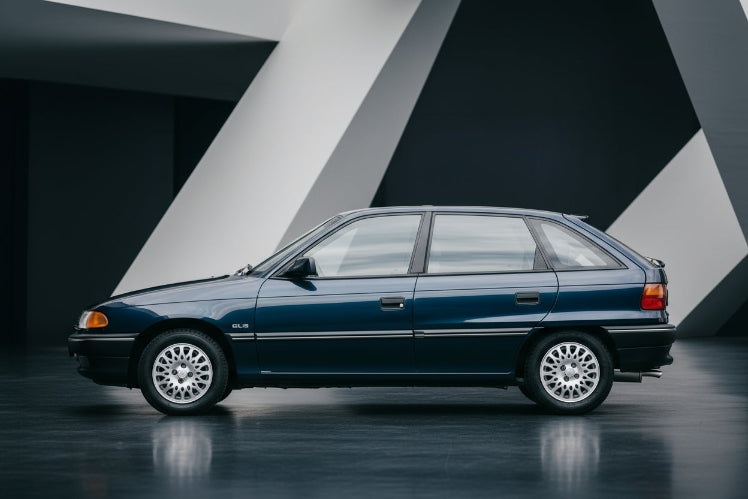 Blue Opel Astra F (1991–1998) on a gray road with a white background